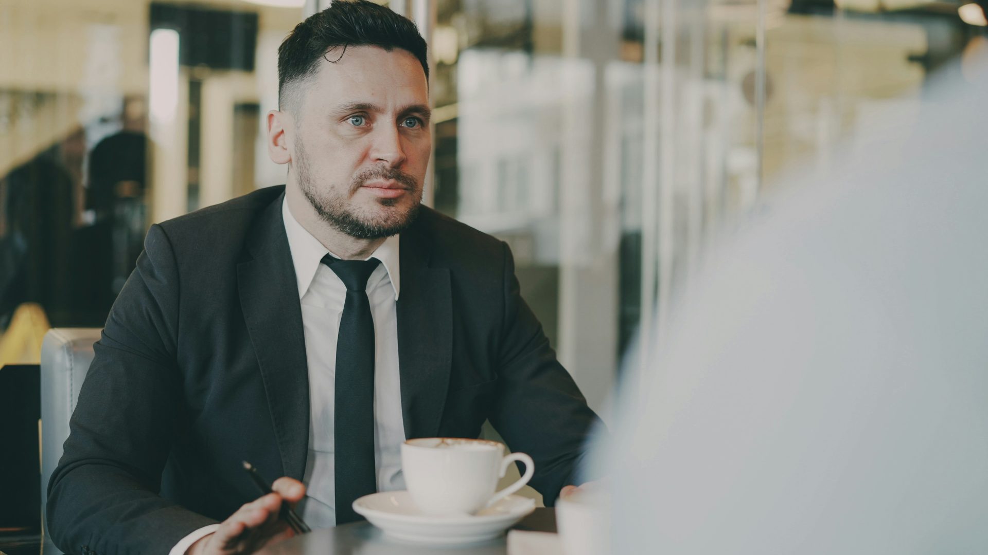 Mann im Anzug unterhält sich mit einer Tasse Kaffee am Tisch.